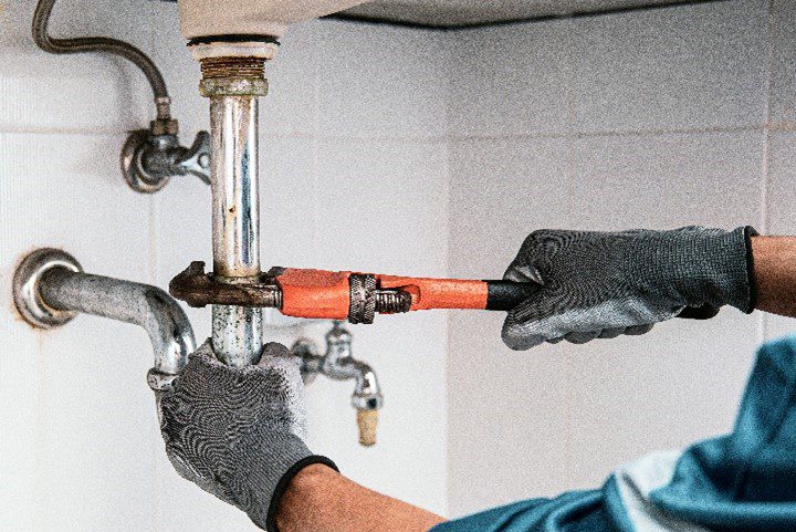 A plumber using a wrench to unclog a blockage from a bathroom sink that requires professional drain cleaning services in Clever, MO. For drain cleaning services, contact your local plumber.