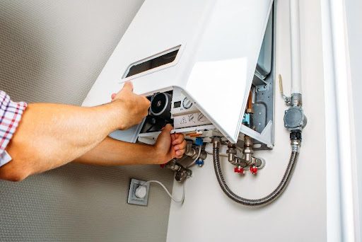 A professional plumber opening the case of a tankless water heater on the wall of a residential home in Republic, MO, to conduct a water heater repair and maintenance service.