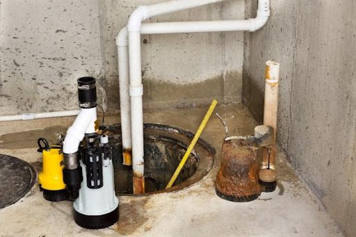 A sump pump being installed by a plumber in a residential basement in Brookline, MO with white pipes.
