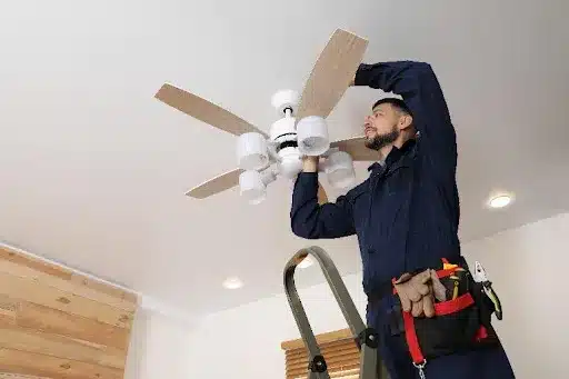 An Electrician in a Brookline, MO, home using tools to install a ceiling fan.