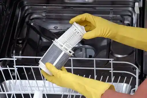 A homeowner’s hands wearing yellow cleaning gloves holds a filter from the dishwasher so it can be inspected and cleaned in Springfield, MO.