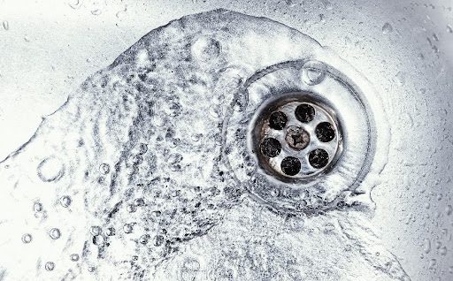 Water flowing into a metal sink drain with visible bubbles.