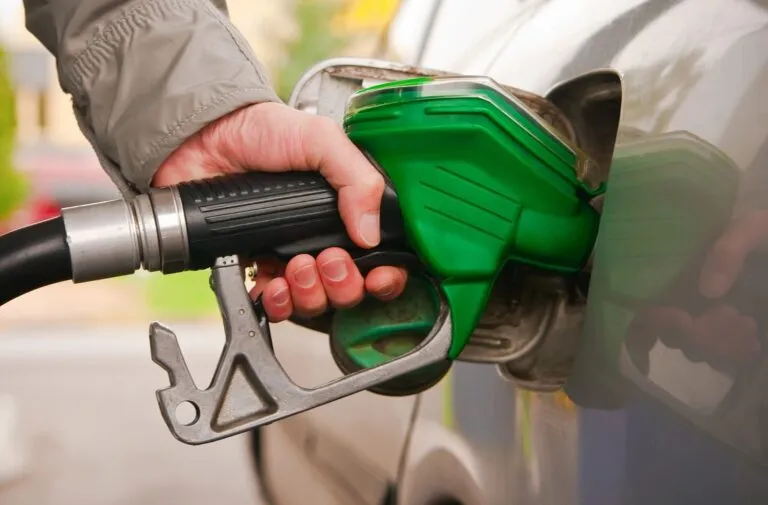 A person refuels a vehicle by inserting a green gasoline nozzle into the gas tank.