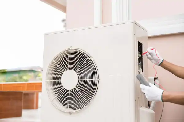 Technician checking an air conditioning unit with a multimeter outdoors.