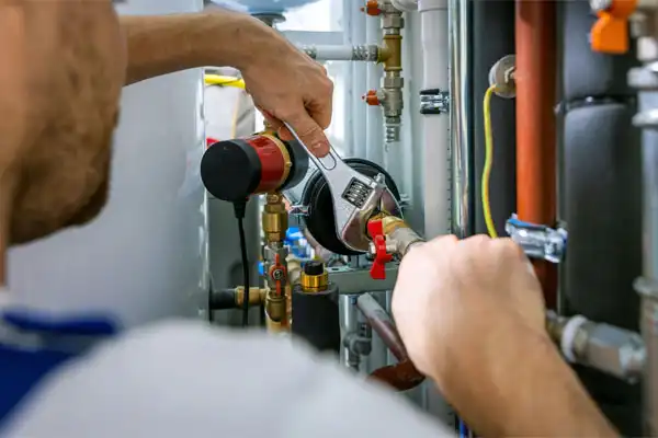 A person uses a wrench to adjust pipes and valves on industrial equipment in a mechanical room.