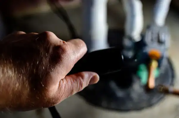 A person holds a black remote control, directing it towards an object with a figure in the background.
