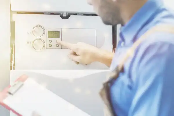 A person in a blue shirt adjusts the settings on a home heating system, while holding a clipboard.