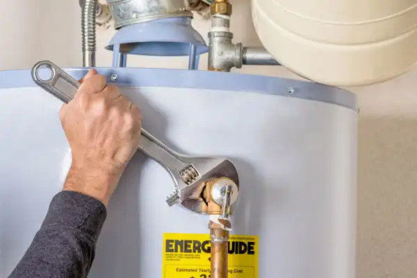 Person using a wrench to adjust a pipe on a water heater, with an energy guide label visible.